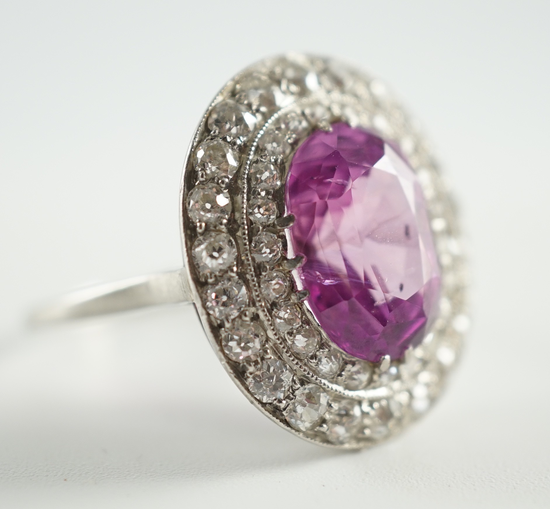 An early 20th century platinum, oval cut purple-pink sapphire and round cut diamond cluster set dress ring